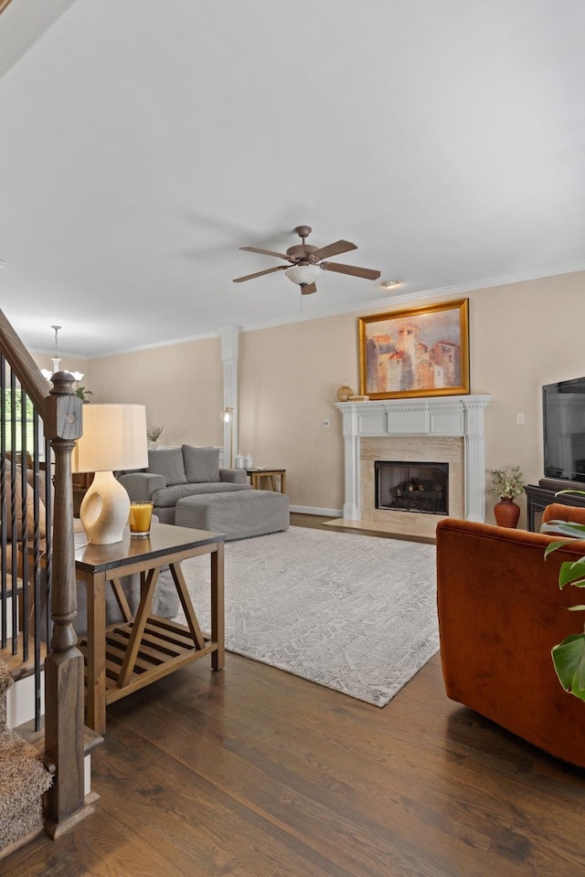 living area with a ceiling fan, wood finished floors, a fireplace, stairs, and ornamental molding