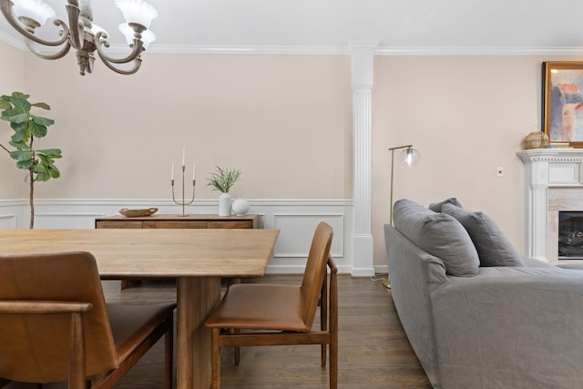 dining room featuring dark wood-type flooring, a chandelier, ornamental molding, wainscoting, and a fireplace