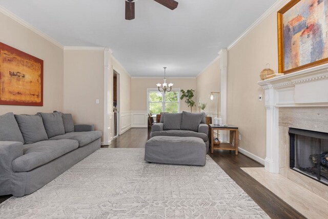 living room featuring dark wood-style floors, ornamental molding, a ceiling fan, a chandelier, and a fireplace