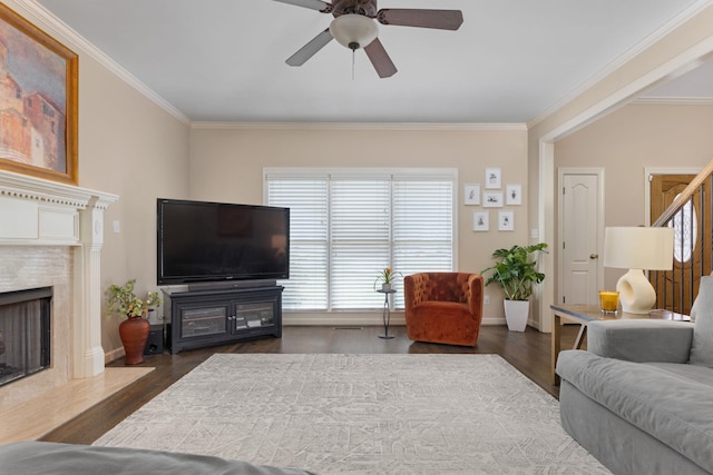 living room with crown molding, a fireplace, ceiling fan, wood finished floors, and baseboards