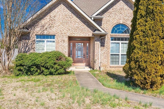 doorway to property featuring a yard, roof with shingles, and brick siding