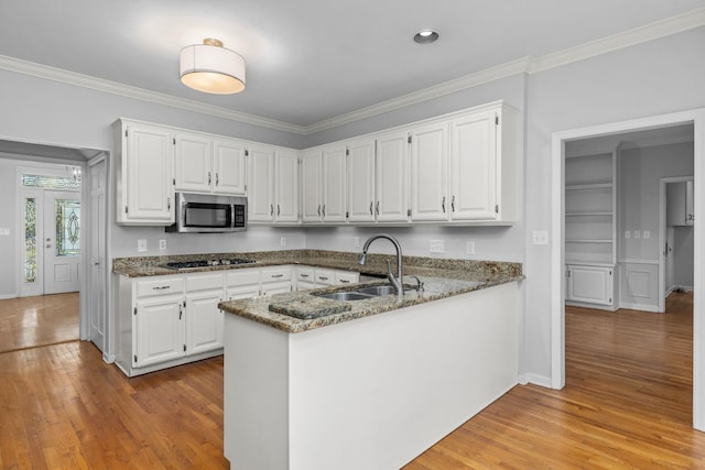 kitchen with sink, white cabinetry, stainless steel appliances, kitchen peninsula, and dark stone counters