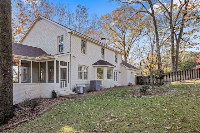 rear view of property featuring central AC unit, a lawn, and a sunroom