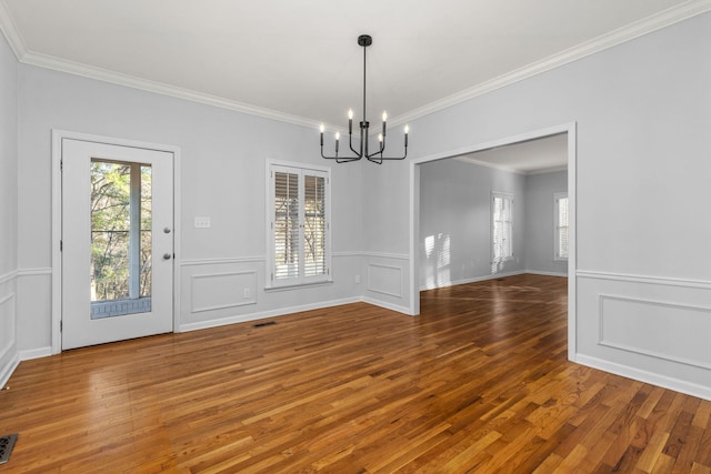 unfurnished dining area with wood-type flooring, ornamental molding, and a notable chandelier