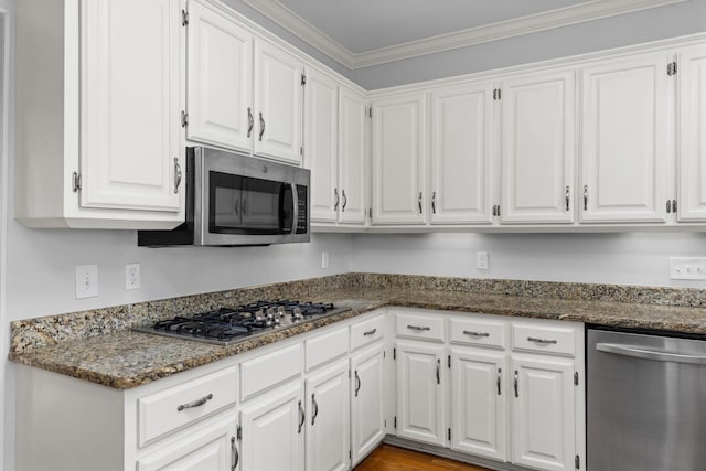 kitchen with white cabinetry, ornamental molding, dark stone counters, and appliances with stainless steel finishes