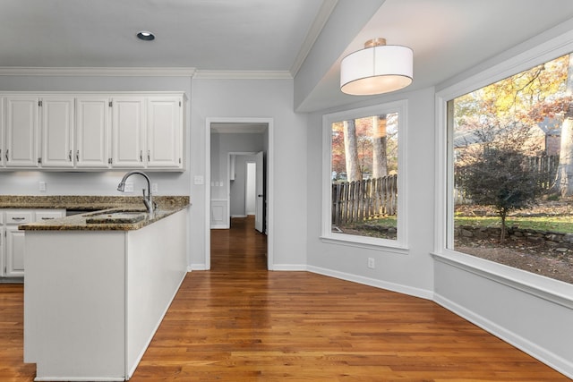 kitchen with white cabinetry, sink, dark stone countertops, ornamental molding, and light hardwood / wood-style flooring