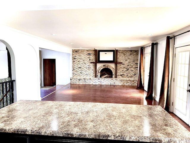 unfurnished living room with ornamental molding, brick wall, dark hardwood / wood-style floors, and a fireplace