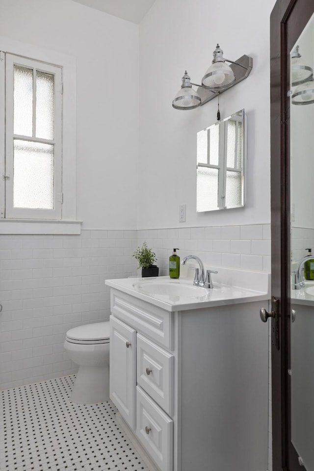  - bathroom featuring tile walls, wainscoting, tile patterned floors, vanity, and toilet