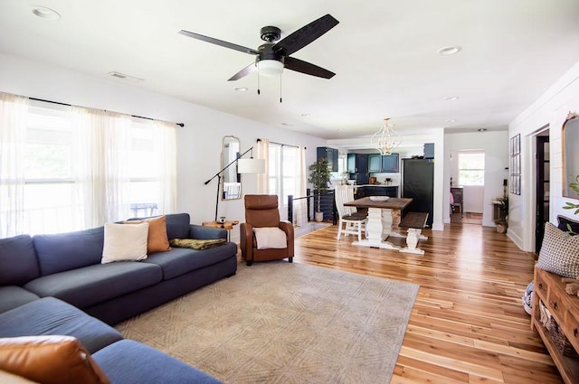 living room with ceiling fan with notable chandelier and light wood-type flooring