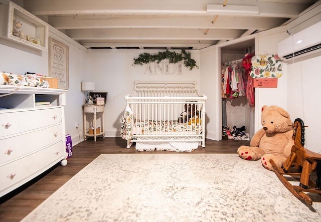 bedroom featuring a crib, dark wood-type flooring, and an AC wall unit