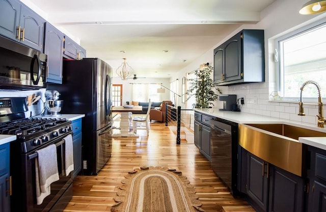 kitchen featuring blue cabinets, sink, light hardwood / wood-style flooring, tasteful backsplash, and stainless steel appliances