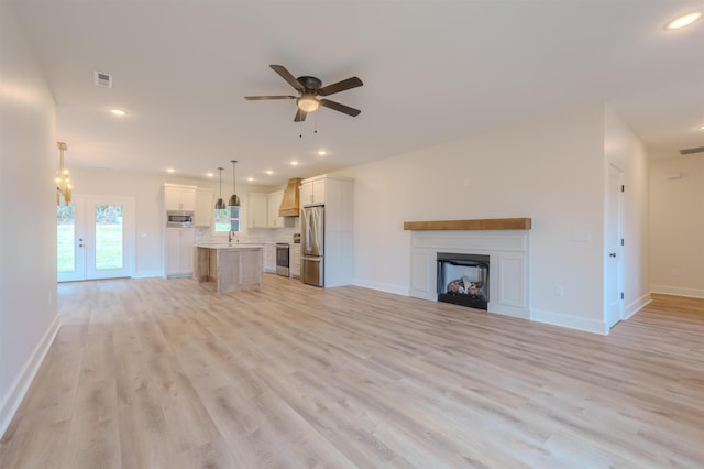 unfurnished living room with ceiling fan, a fireplace, visible vents, baseboards, and light wood-type flooring