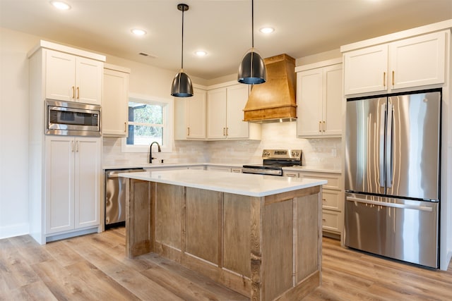 kitchen with wall chimney exhaust hood, appliances with stainless steel finishes, light countertops, light wood-type flooring, and a sink