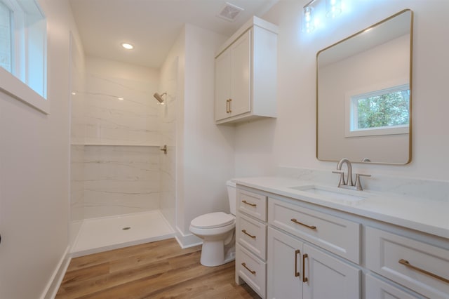 bathroom with a marble finish shower, visible vents, toilet, wood finished floors, and vanity