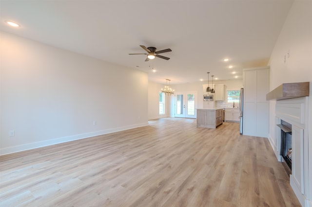 unfurnished living room with baseboards, light wood-style flooring, ceiling fan with notable chandelier, a fireplace, and recessed lighting