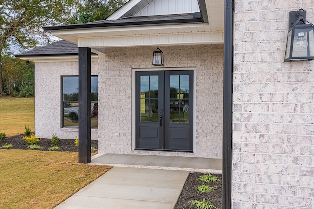 entrance to property with french doors, a lawn, a shingled roof, and brick siding