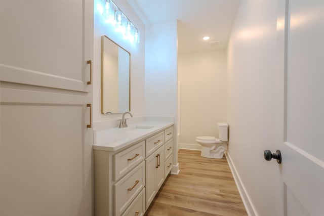 bathroom with recessed lighting, toilet, vanity, wood finished floors, and baseboards