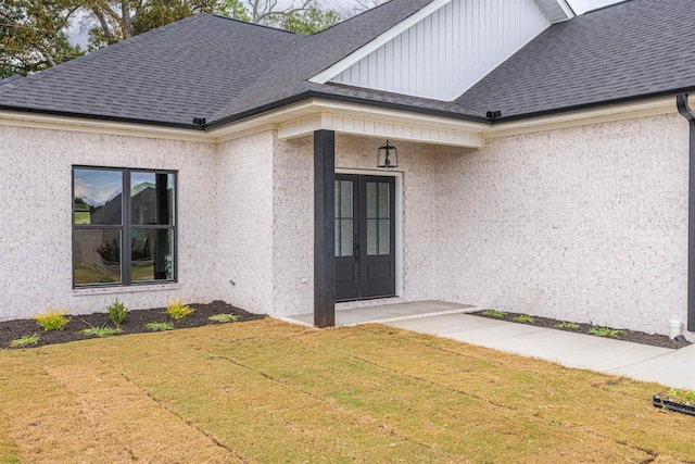 entrance to property featuring a yard, french doors, and roof with shingles