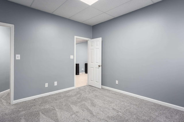 spare room featuring a drop ceiling, carpet, and baseboards