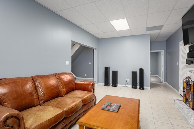 living area with a paneled ceiling, a brick fireplace, baseboards, and light tile patterned floors