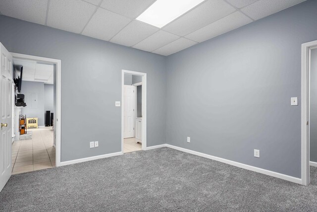 carpeted empty room featuring a drop ceiling, tile patterned flooring, and baseboards