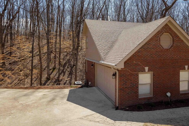 exterior space with brick siding, driveway, an attached garage, and roof with shingles