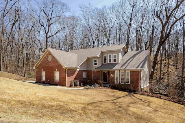 view of front of house featuring brick siding, a shingled roof, and a front yard