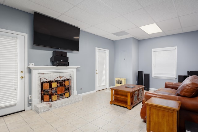 living room with a drop ceiling, a fireplace, light tile patterned flooring, and baseboards