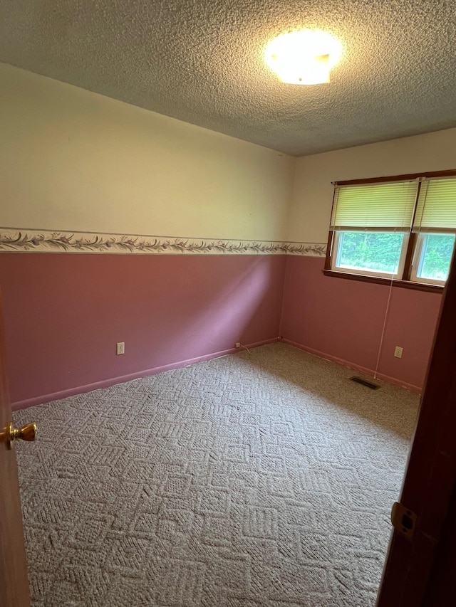 empty room featuring a textured ceiling, visible vents, baseboards, and carpet floors