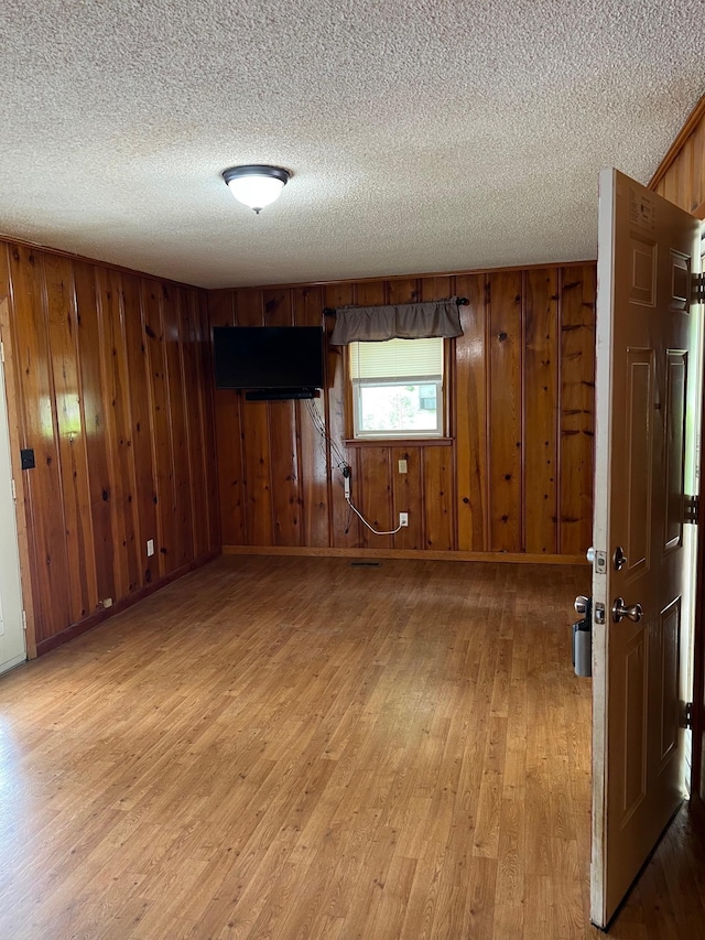 spare room featuring wooden walls, light wood finished floors, and a textured ceiling