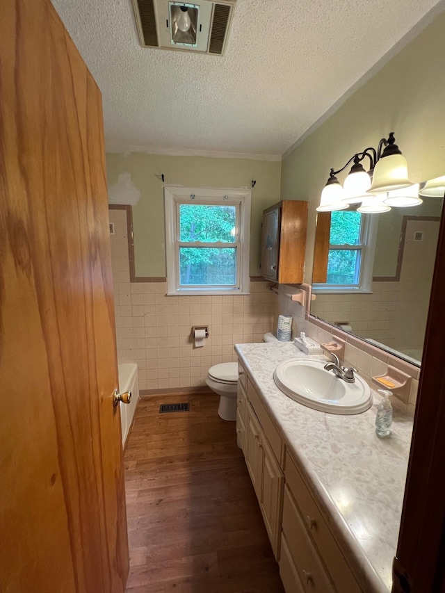 full bathroom with tile walls, plenty of natural light, wood finished floors, and toilet