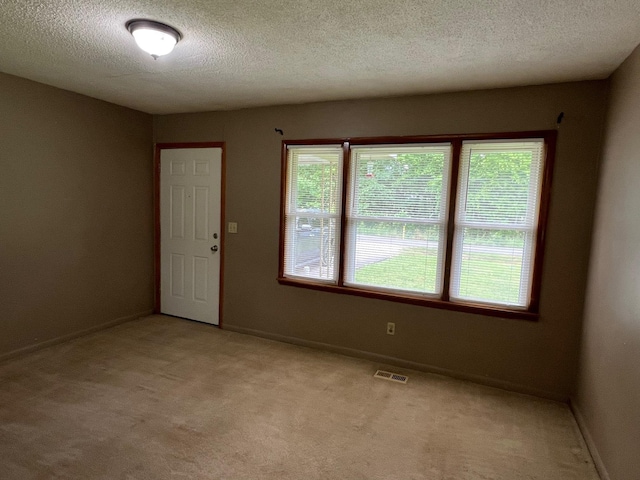 spare room featuring a textured ceiling, baseboards, visible vents, and light colored carpet