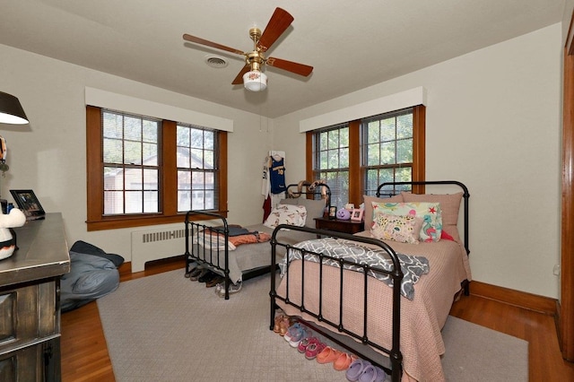 bedroom with ceiling fan, wood-type flooring, and radiator