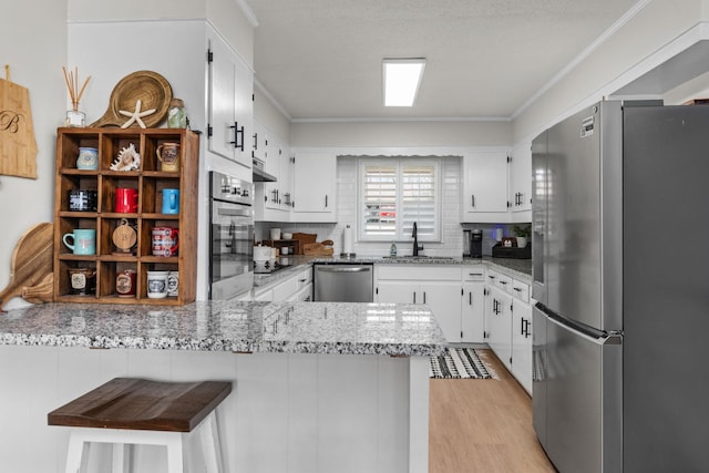 kitchen with sink, stainless steel appliances, light stone counters, white cabinets, and kitchen peninsula