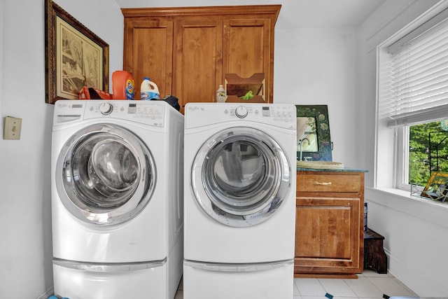 clothes washing area featuring separate washer and dryer, light tile patterned flooring, and cabinets