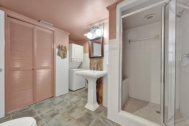 bathroom with a shower with door, crown molding, stacked washer and clothes dryer, tile patterned flooring, and toilet