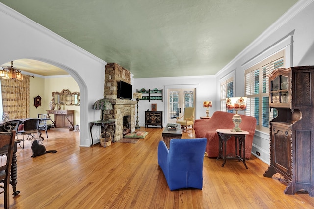 living room featuring french doors, crown molding, light wood-type flooring, a fireplace, and a chandelier