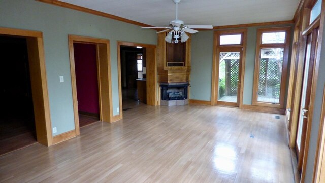  - unfurnished living room featuring light wood finished floors, a fireplace, a ceiling fan, baseboards, and crown molding