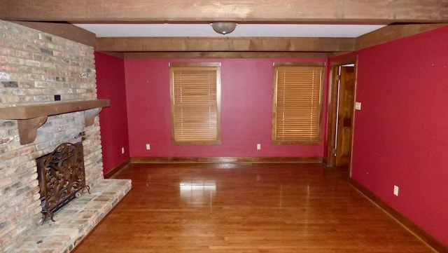  - unfurnished living room featuring beamed ceiling, a fireplace, wood finished floors, and baseboards