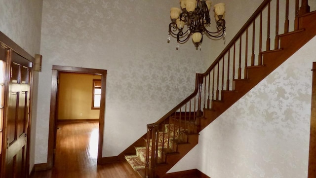  - stairway featuring wood finished floors, a towering ceiling, baseboards, and a chandelier