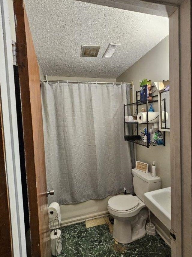  - full bath with toilet, shower / bath combo, a textured ceiling, and a sink