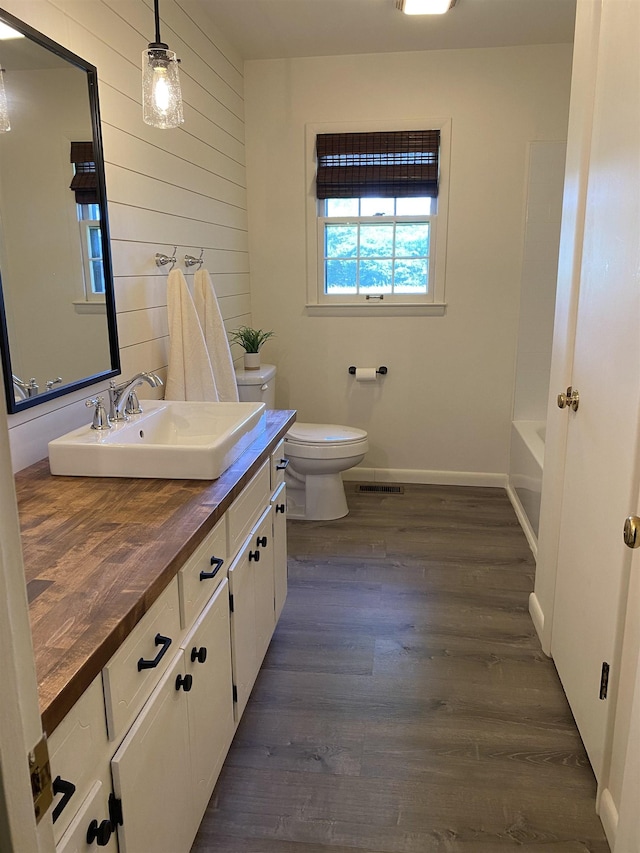  - full bath featuring toilet, wood finished floors, vanity, a bathtub, and wood walls