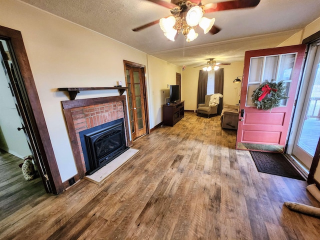 living room with a textured ceiling, hardwood / wood-style flooring, a brick fireplace, and ceiling fan