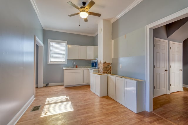 kitchen with light wood-type flooring, white cabinetry, ceiling fan, and sink