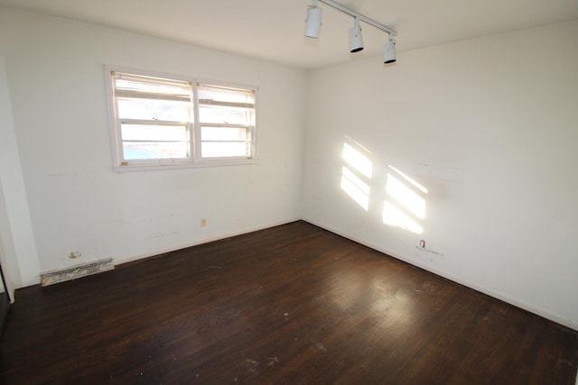 empty room with dark hardwood / wood-style flooring and track lighting