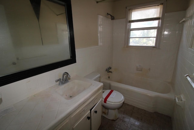 full bathroom with tile walls, tiled shower / bath, vanity, and toilet