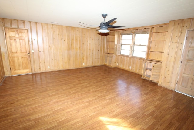 unfurnished room with hardwood / wood-style floors, wooden walls, and ceiling fan