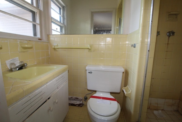 bathroom with tile walls, vanity, toilet, and a tile shower