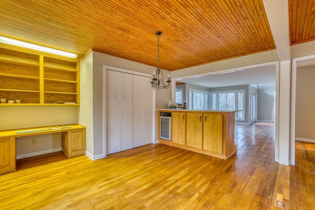 kitchen featuring decorative light fixtures, built in desk, light wood-type flooring, kitchen peninsula, and beverage cooler