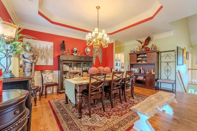 dining area with a chandelier, light hardwood / wood-style floors, ornamental molding, and a tray ceiling